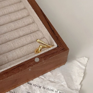 Macro shot of a minimalist gold twisted U-shaped ring on a wooden jewelry display case
