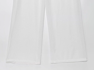 Detailed view of white wide-leg trousers showing lightweight textured fabric and clean hem