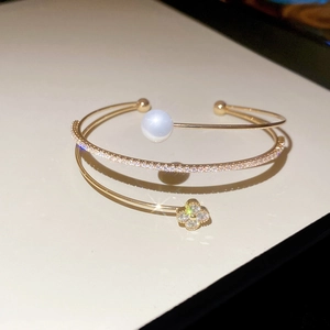 Detail of a three-layer gold open bangle featuring a pearl and sparkling clover motif