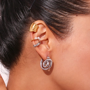 Macro detail of stacked 18K gold C-shaped earrings and textured ear cuff on model