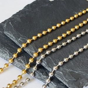 Detailed view of polished gold and silver metal bead chains on a dark stone background