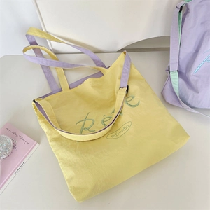 Detailed macro view of yellow and purple nylon tote bag featuring embroidered text