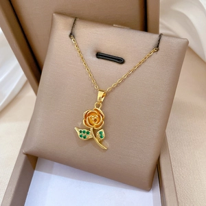 Detailed shot of golden rose pendant with green gemstone on a soft silk background
