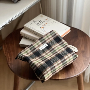 Detailed texture of green plaid tweed makeup bag on a wooden stool in a cozy setting
