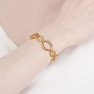 Detailed close-up of a gold geometric oval link chain bracelet on a female wrist