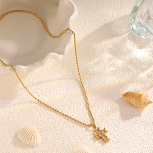 Detail of a gold cross pendant with zircons on a twisted rope chain over sandy background