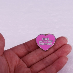 Pink heart enamel pin with soulmate quote held in hand against a white background