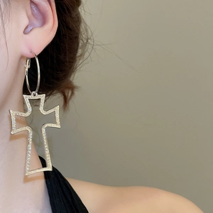 Detailed macro view of large textured silver cross pendant earrings worn by a model