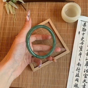 Close-up of a translucent green glass bangle on a wrist with traditional Chinese decor