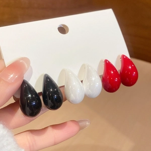 Close-up of three pairs of glossy teardrop earrings in black, white, and vibrant red