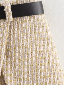 Macro detail of cream tweed fabric with gold threads and a black leather belt