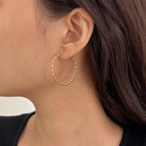 Detailed view of polished gold twisted hoop earrings worn by a model in soft light