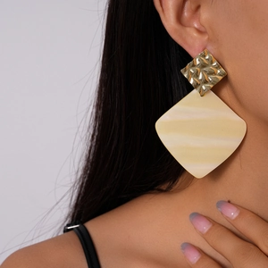 Close-up of geometric diamond earrings with gold hammered metal and cream resin charms