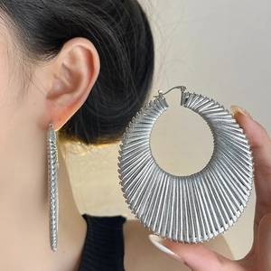 Boucles d'oreilles créoles géantes argentées à texture plissée portées par un mannequin