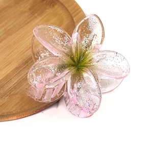 Detail of pink translucent frangipani hair claw clip with silver glitter and green center