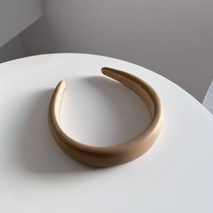 Top-down view of a beige padded PU leather wide headband on a minimalist white table