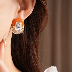 Detail of vintage oval earring with orange enamel and sparkling crystals on model