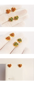 Close-up of heart-shaped gold studs with red and green cubic zirconia on a knit surface