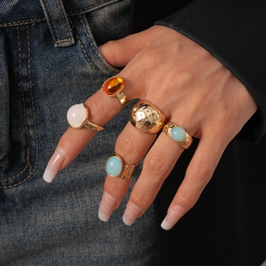 Close-up of five-piece gold ring set with resin gemstones on model's hand with French nails