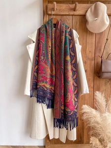 Detail of colorful paisley shawl with fringes on white wool coat and wood hanger
