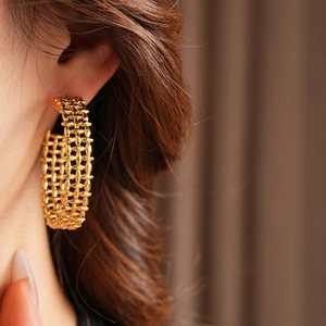 Detailed close-up of chunky gold-toned braided hollow C-shape hoop earrings on a model