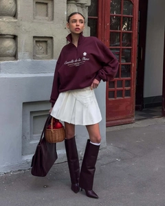 Detailed view of burgundy half-zip sweatshirt with white pleated skirt and tall boots