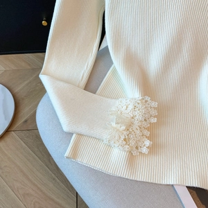 Vue détaillée d'un pull en maille crème avec poignets en dentelle et texture côtelée