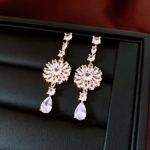 Macro view of gold flower drop earrings with clear zircon crystals on black leather