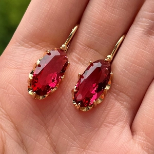 Macro view of gold-plated oval red ruby earrings with multi-prong setting held in hand