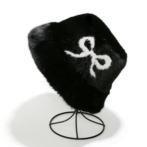 Detail of plush black faux fur bucket hat with white bow pattern and soft winter texture
