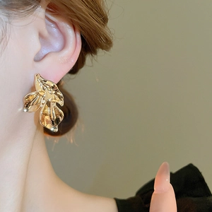 Macro detail of gold-plated irregular petal stud earring with metallic texture on ear