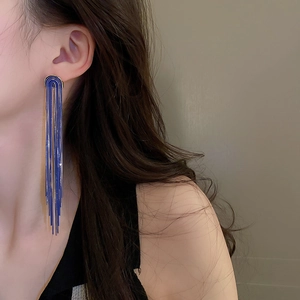 Detail of long blue and gold U-shaped chain tassel earrings on a model showing metallic sheen