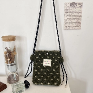 Close-up of olive green plush crossbody bag with white heart pattern and braided strap
