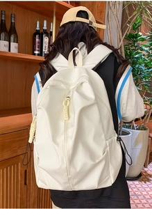 Detailed view of white minimalist backpack featuring vertical zippers and woven charms