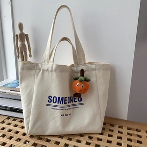 Detail of off-white canvas tote bag with blue lettering and cute persimmon plush charm