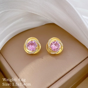 Macro shot of gold stud earrings with a pink crystal center and white diamond spiral accents