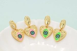 Macro shot of colorful heart evil eye earrings in pink and green enamel with gold plating