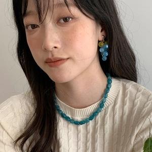 Close-up of elegant blue resin grape earrings and teal beaded necklace on a model