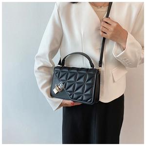 Détail d'un sac à main noir matelassé avec fermoir doré sur un blazer blanc élégant