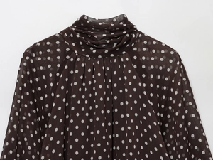 Detailed view of brown polka dot blouse featuring a high ruffled collar and chiffon texture