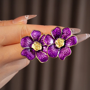 Primer plano de pendientes de flores en esmalte púrpura vintage con bordes dorados