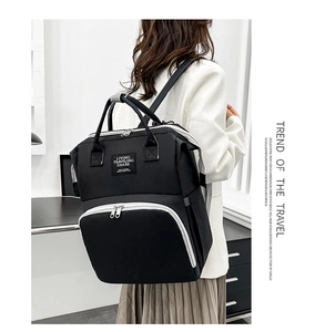 Rear view of a black Oxford cloth diaper bag with contrasting white zippers and handles