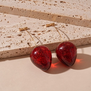 Detail shot of cherry earrings with sparkling red resin spheres and curved gold metal stems