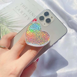 Hand holding heart shaped holographic glitter phone grip on a green smartphone