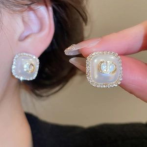 Close-up of square pearl earrings with gold initials and sparkling crystal border