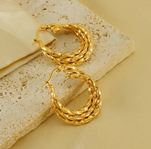 Detailed view of layered twist hoop earrings in 18K gold finish on silk fabric