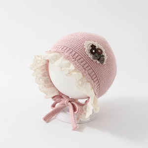 Detailed knit texture of pink baby bonnet with white lace trim and floral bow applique