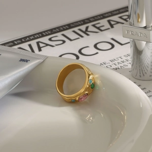 Macro shot of gold wide band ring with colorful zircon stones on white ceramic tray