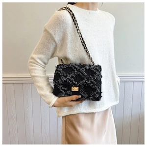Detail of black tweed crossbody bag with gold chain strap and decorative fringe accents