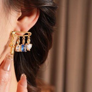 Close-up of golden pin earring featuring blue zircon and cross pendant on model